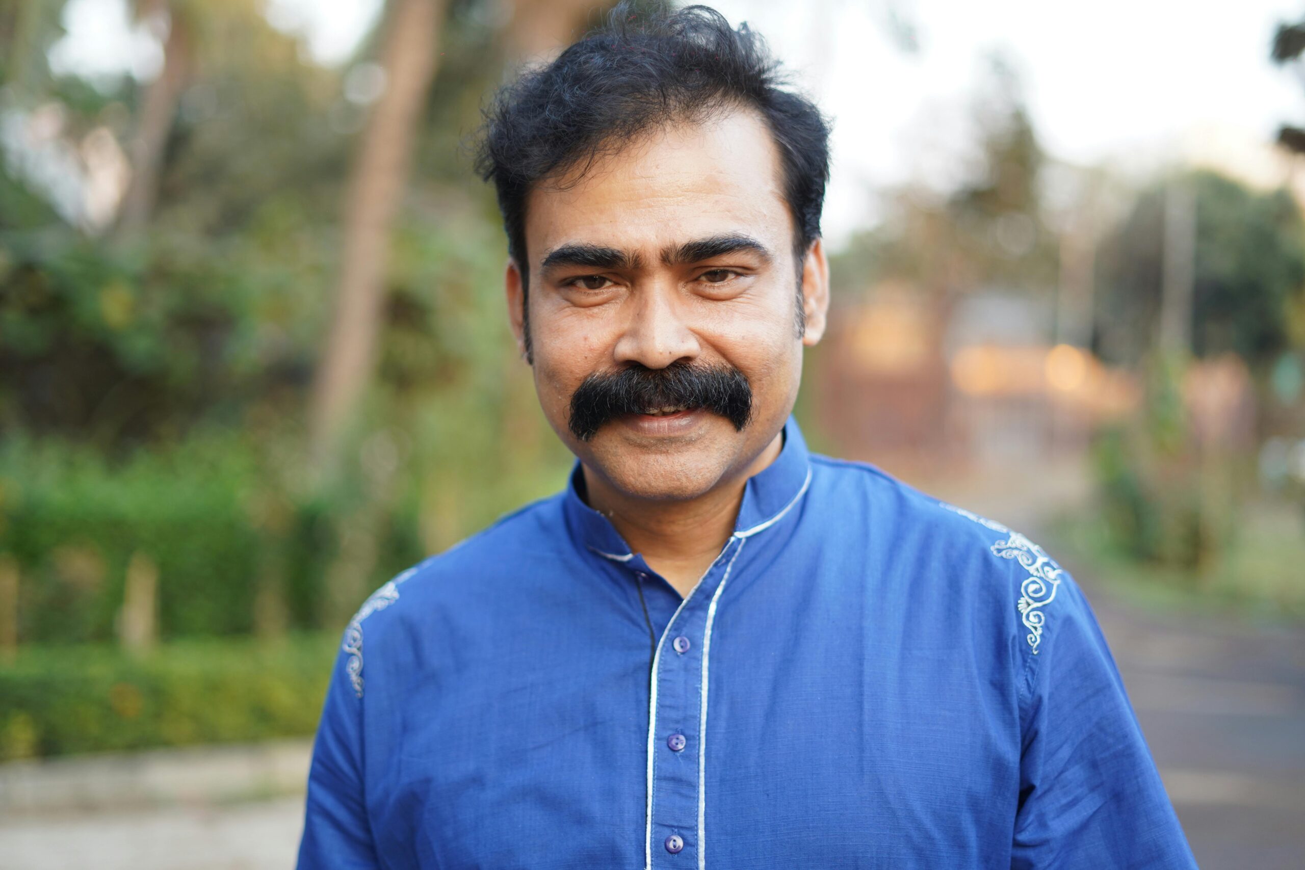 Portrait of a happy man with mustache smiling outdoors in a blue shirt.
